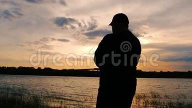 剪影渔夫在背景黄昏日落时在河中投掷鱼竿。 钓鱼时傍晚美丽的日落